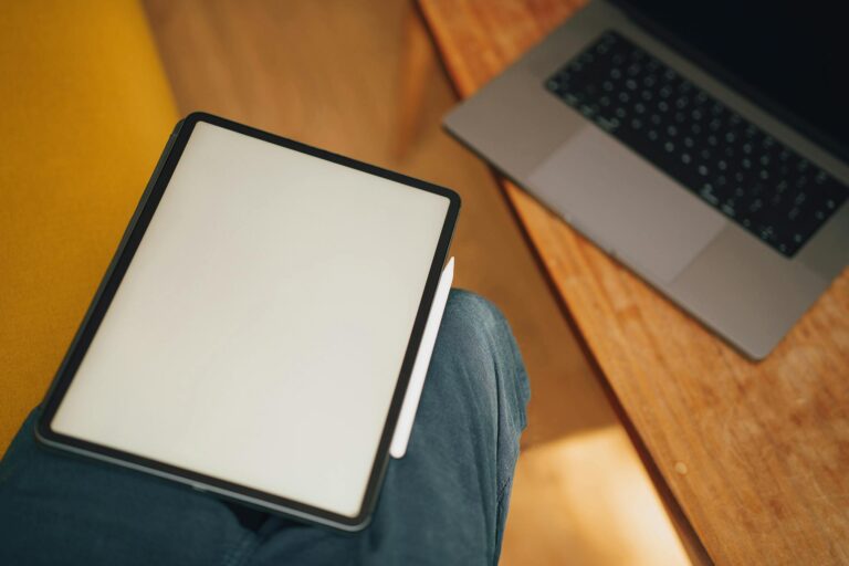 A digital tablet on a lap next to a laptop on a wooden table, ideal for work or study.